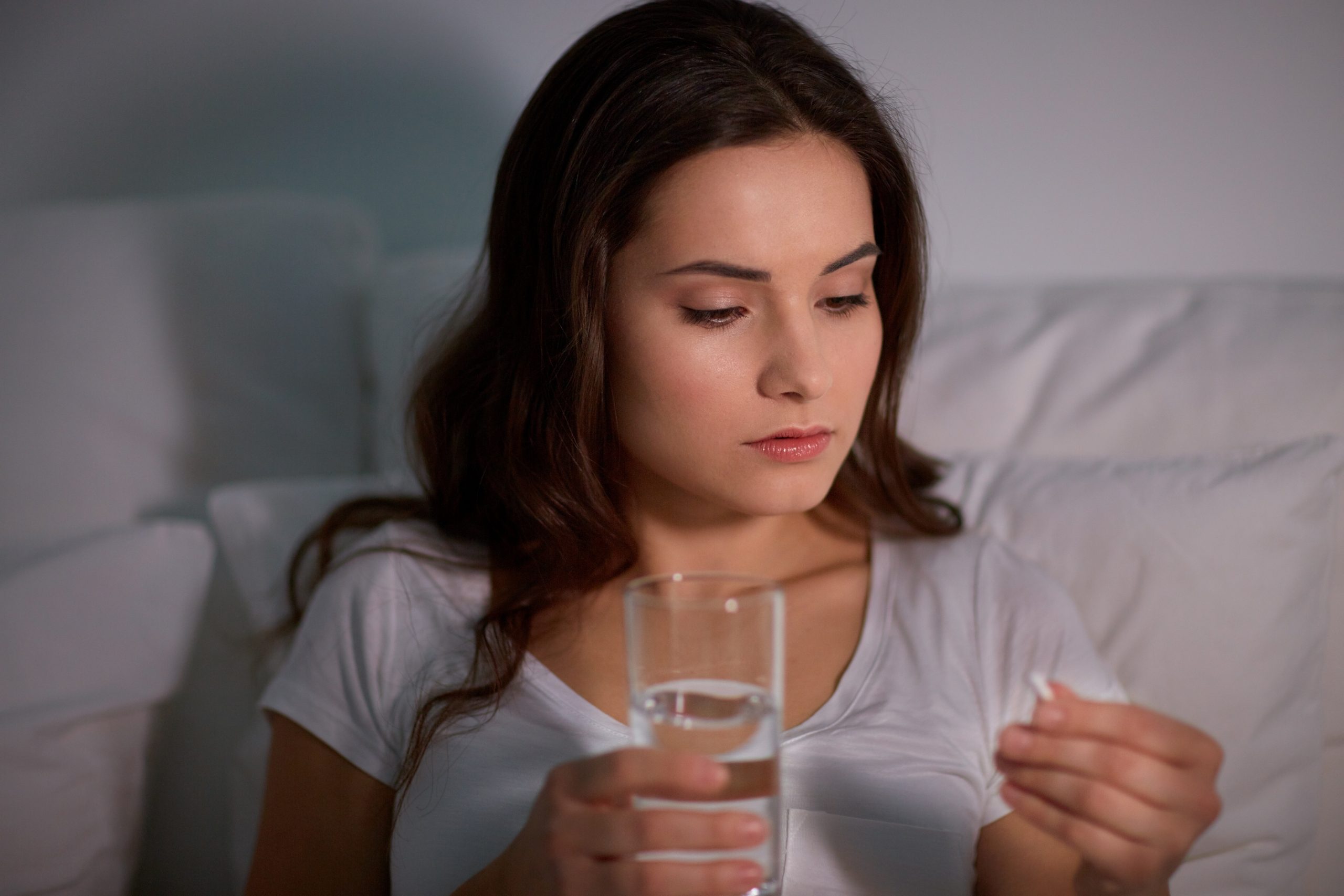 Woman taking sleeping pill with water in bed. Detox from Sleeping pill concept image